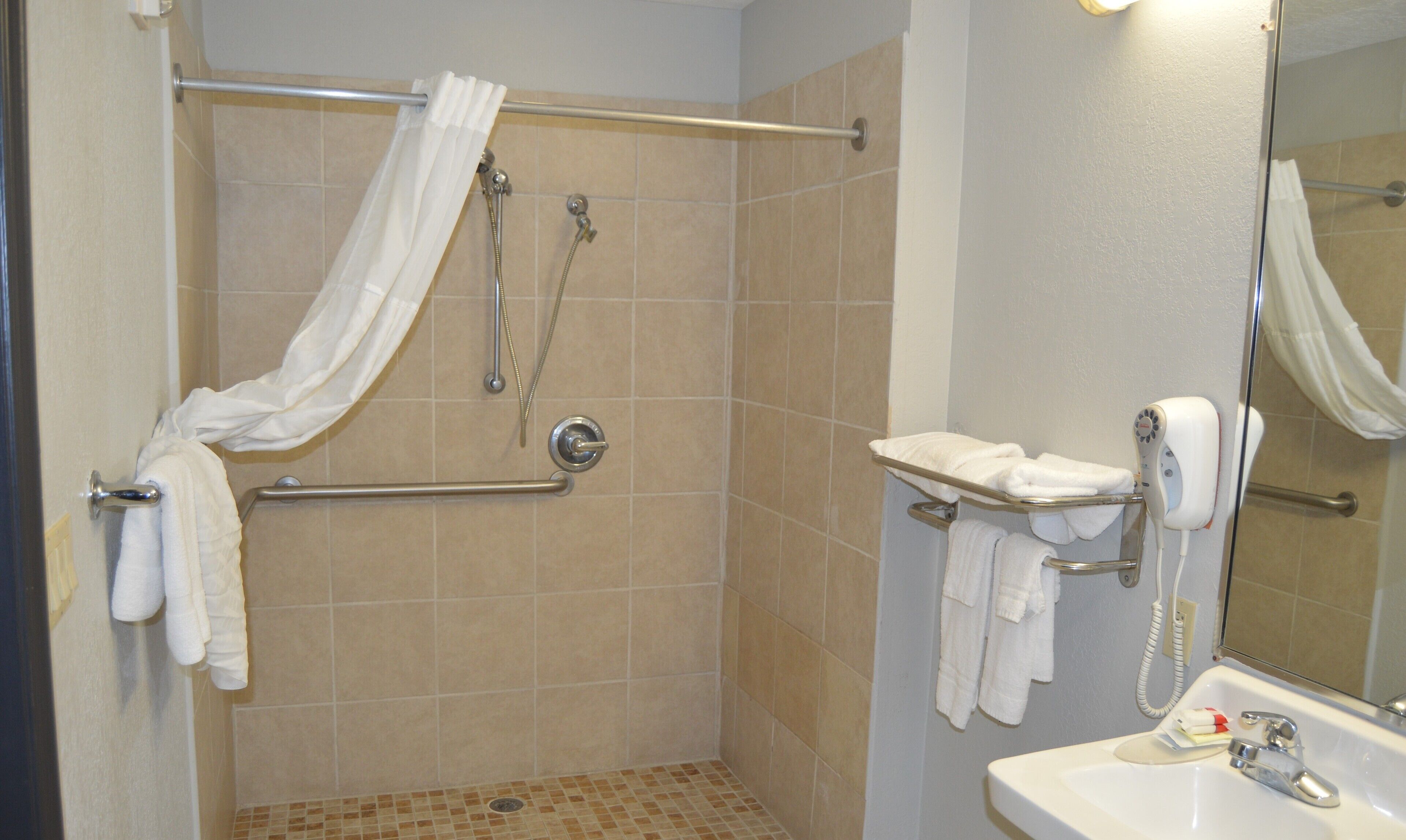Un baño con ducha, secamanos, lavamanos y espejo.