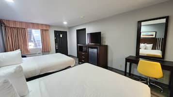 A hotel room with two beds, a desk with a television, a mirror, and a yellow chair.