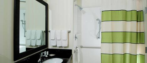 A bathroom with a black sink, white tiles, a large mirror, and a shower curtain with green and beige stripes.