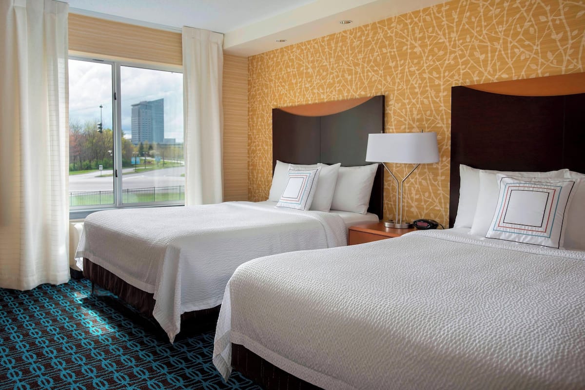 A hotel room with two beds, a large window, and a patterned carpet.