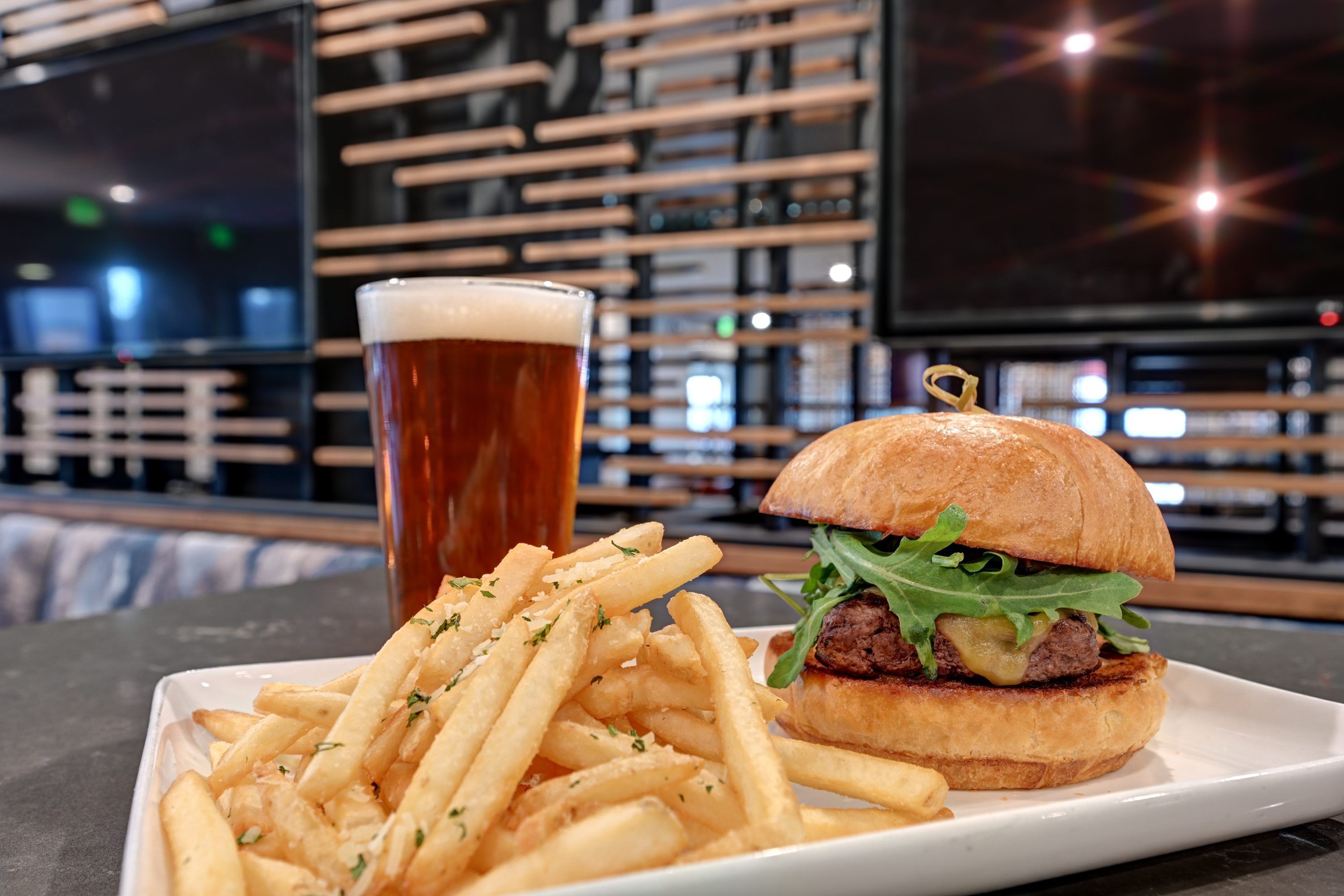 Una hamburguesa con papas fritas y una cerveza en un plato blanco.
