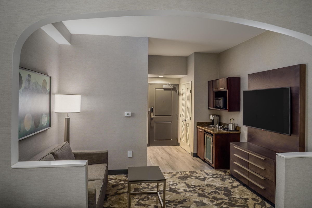A compact living space with a sofa, a small table, a TV, and a kitchenette.