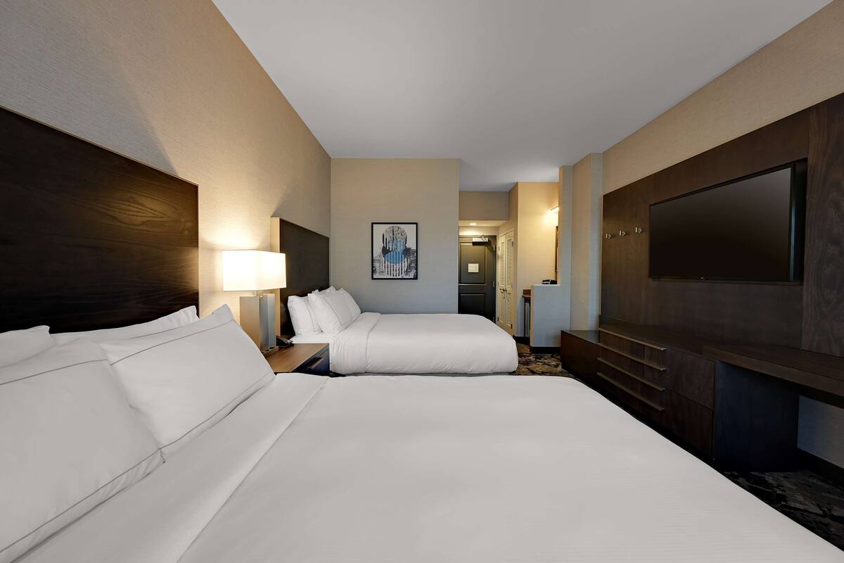 A hotel room with two beds, a TV, a desk, and a painting on the wall.