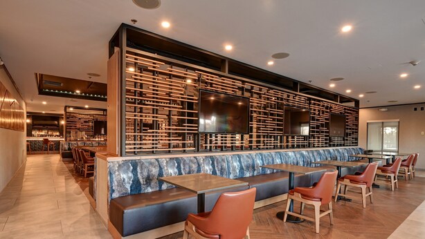 A modern restaurant with a long counter, cushioned seating, and a large TV screen. - DoubleTree by Hilton Denver International Airport (Denver)