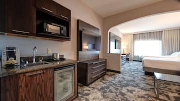 A hotel room with a kitchenette, a large bed, a TV, and a view of the city.