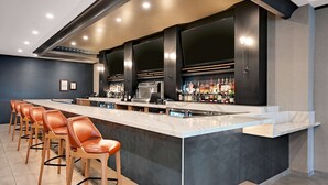 A modern bar area with a long counter, multiple stools, and a variety of bottles. - DoubleTree by Hilton Denver International Airport (Denver)