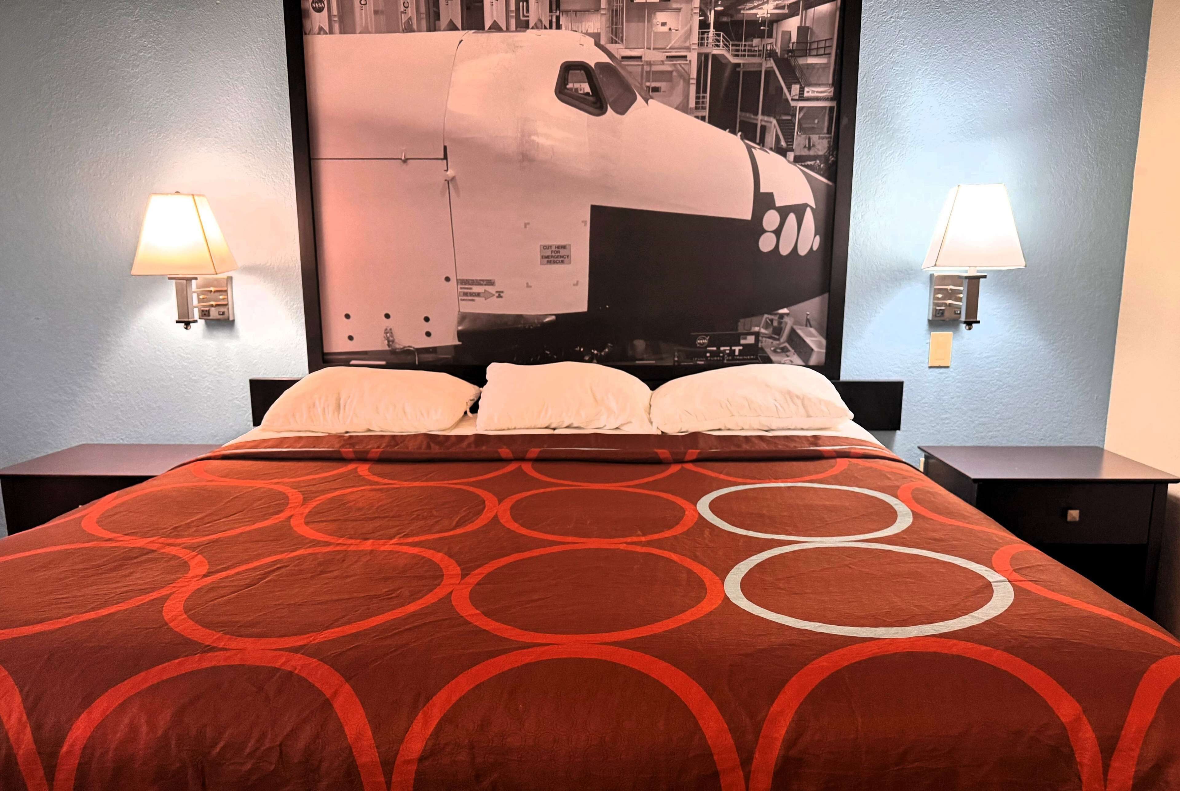 A hotel room with a large bed, two bedside lamps, and a wall-mounted artwork of a train.
