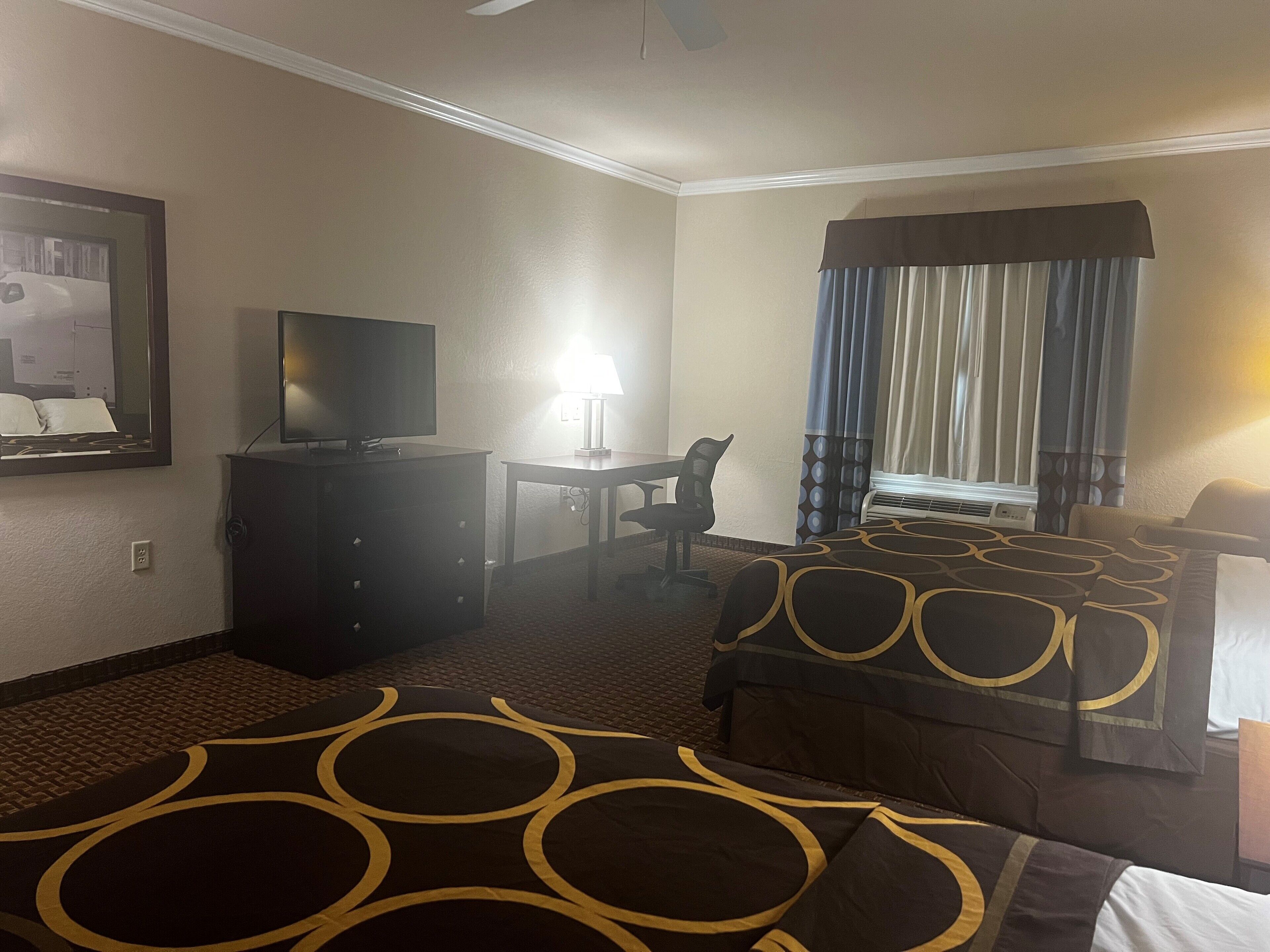 Een hotelkamer met een bed, een bureau met stoel, een televisie en een raam met gordijnen.