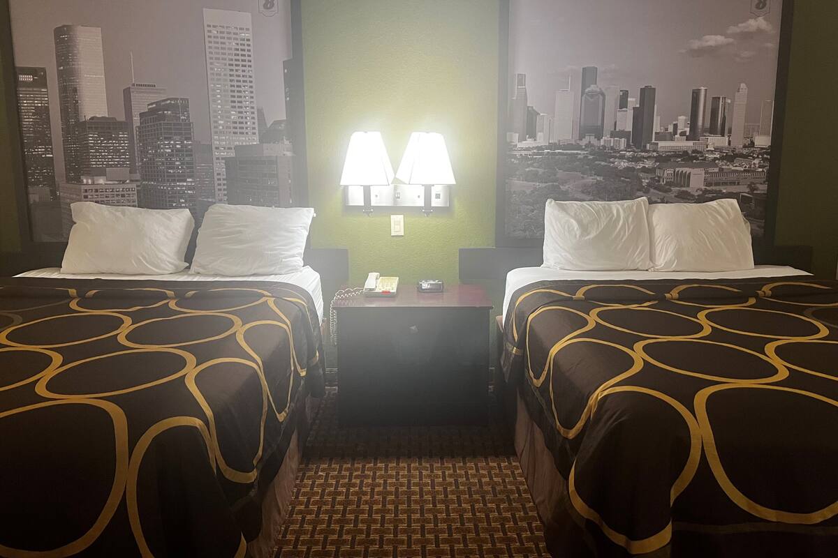 Une chambre d’hôtel avec deux lits, une vue sur la ville, un sol décoré de motifs en briques et une table de chevet avec une lampe et un téléphone.