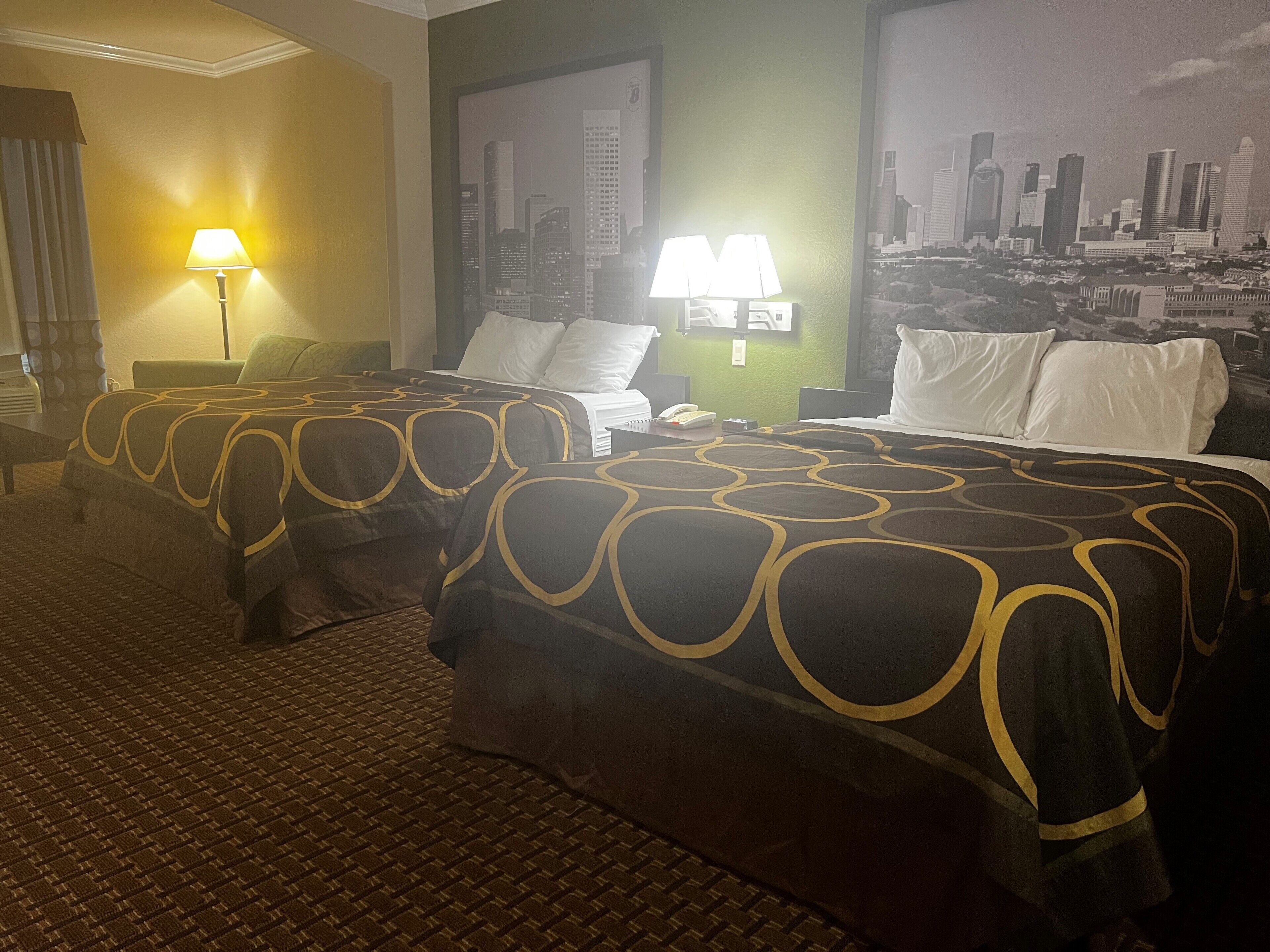 A hotel room with two beds, a cityscape mural, and a brick-patterned floor.