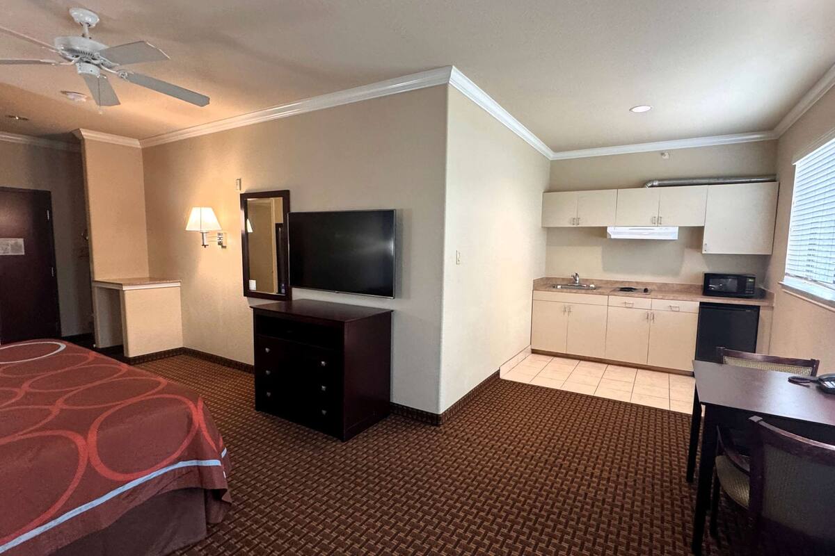 Une chambre d’hôtel équipée d’un lit, d’une télévision, d’un bureau, d’une chaise, d’une kitchenette et d’un ventilateur de plafond.