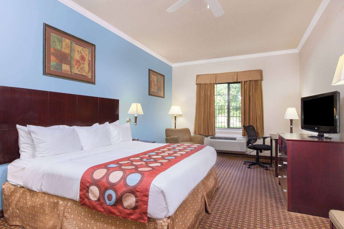 Une chambre d’hôtel avec un grand lit, deux tables de chevet avec des lampes, un bureau avec une télévision et une fenêtre avec des rideaux.