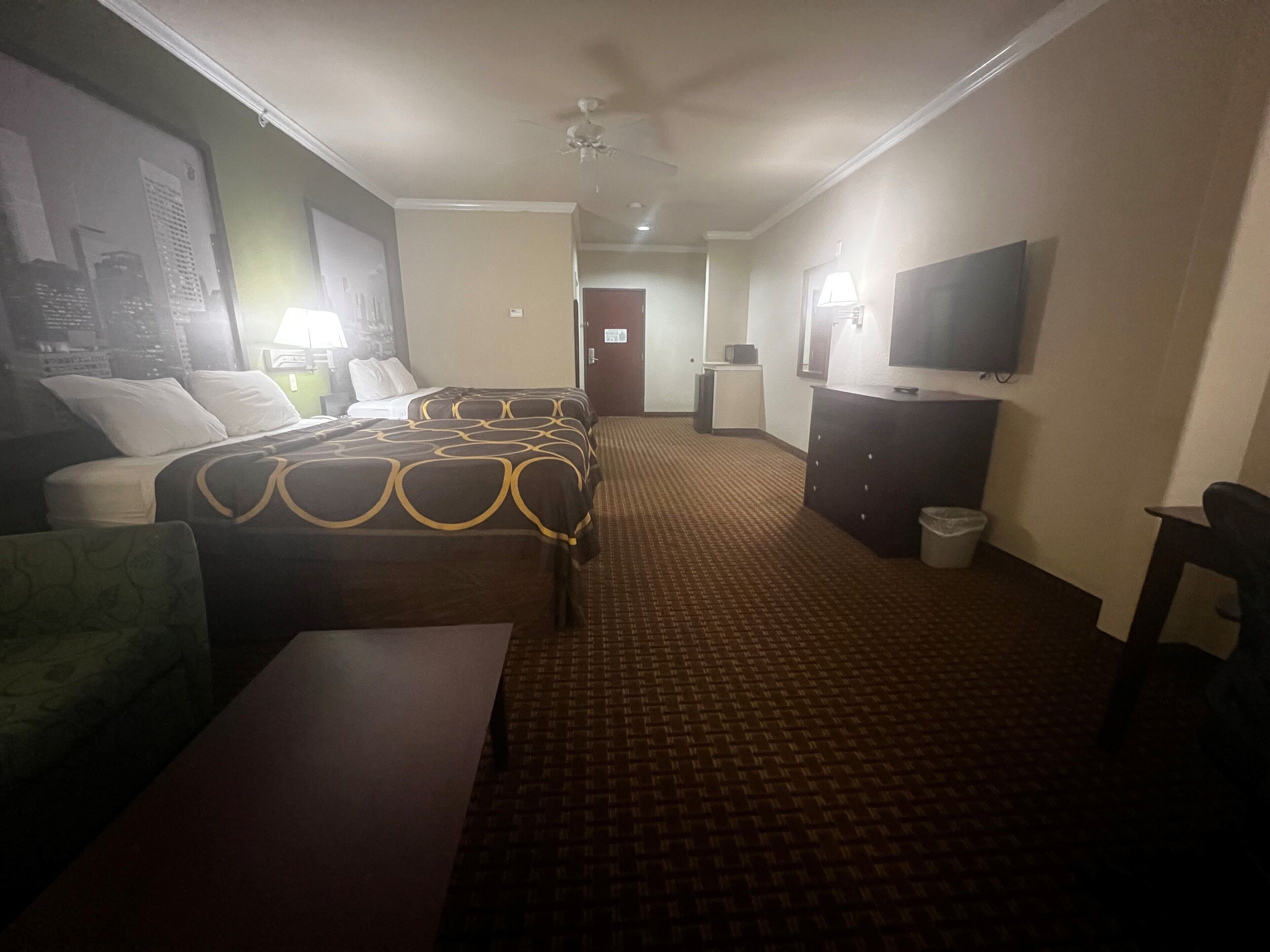 Habitación de hotel con dos camas, un escritorio, una silla, un televisor, una lámpara y un cesto de basura.
