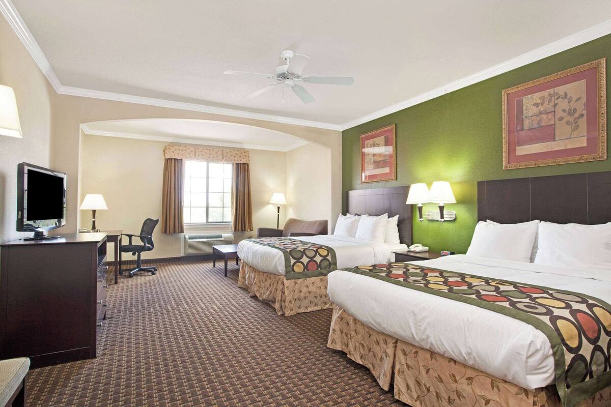Une chambre d’hôtel avec deux lits, un bureau, une chaise, une télévision et un ventilateur de plafond.