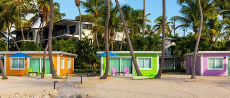 A beachfront property with colorful cottages, palm trees, and a clear sky.