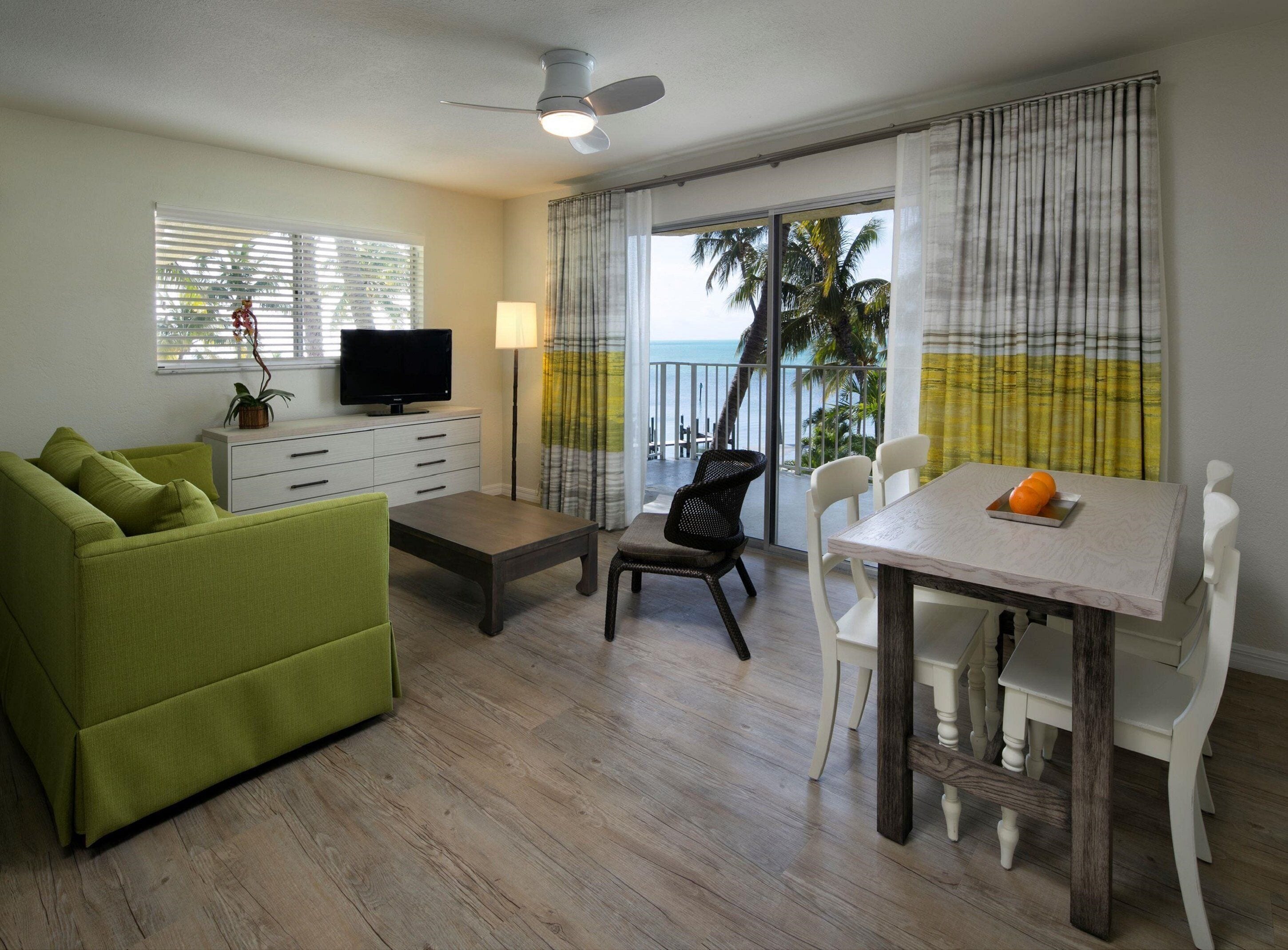 A living room with a green sofa, a coffee table, a TV, and a dining area with a table and chairs.