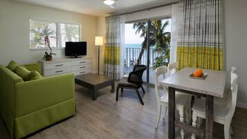 A living room with a green sofa, a coffee table, a TV, and a dining area with a table and chairs.