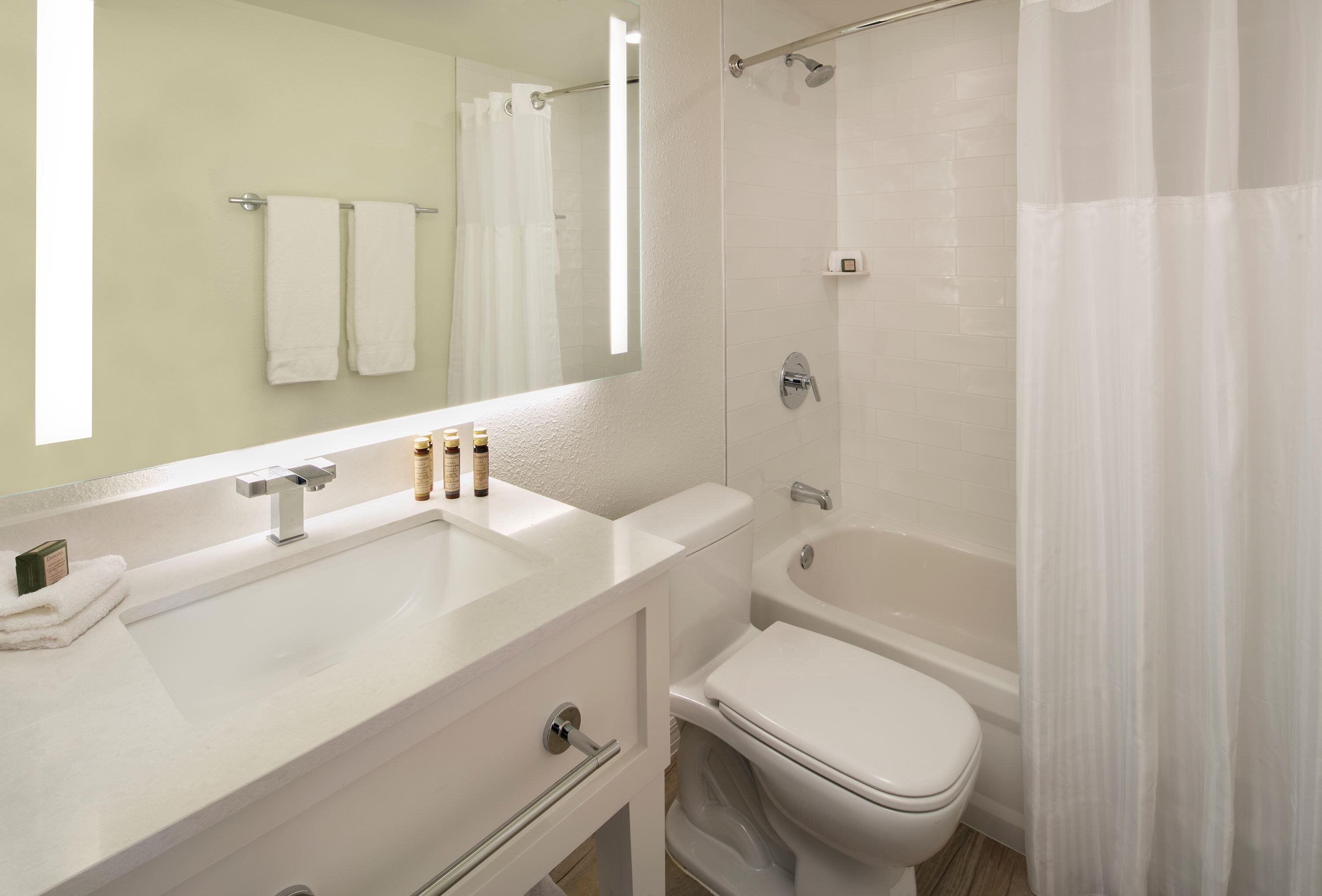 A modern bathroom with a white sink, mirror, and toilet. There are two towels hanging on the wall, and a shower curtain is partially visible.