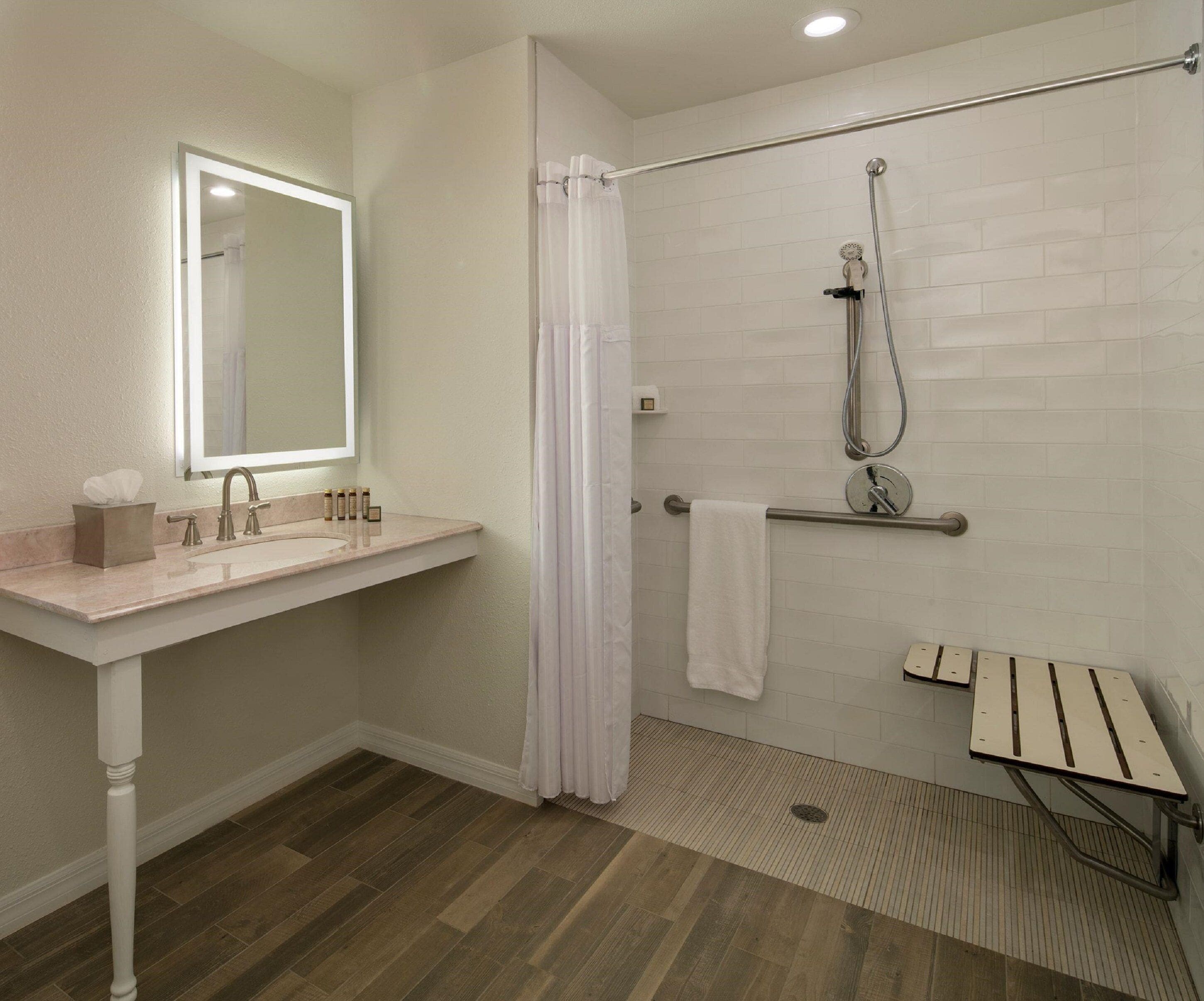 A modern bathroom with a sink, mirror, shower, and a wooden floor.