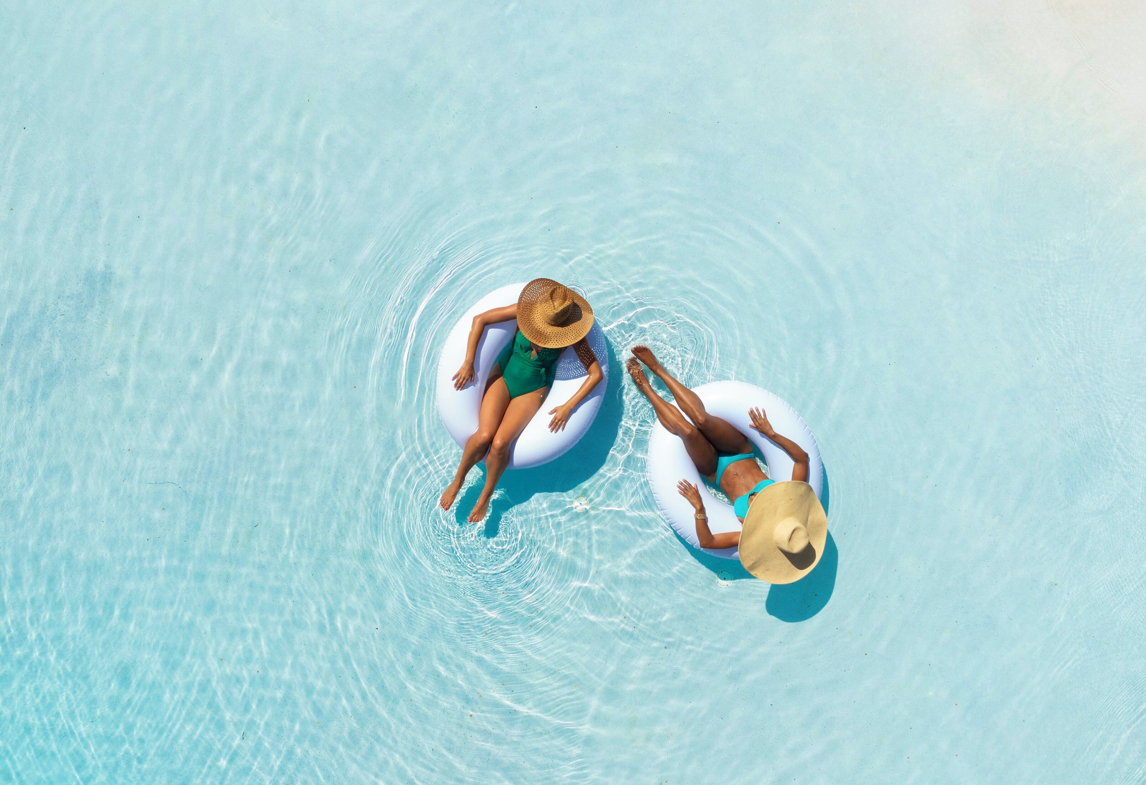 Two people floating on inflatable rings in a clear pool.