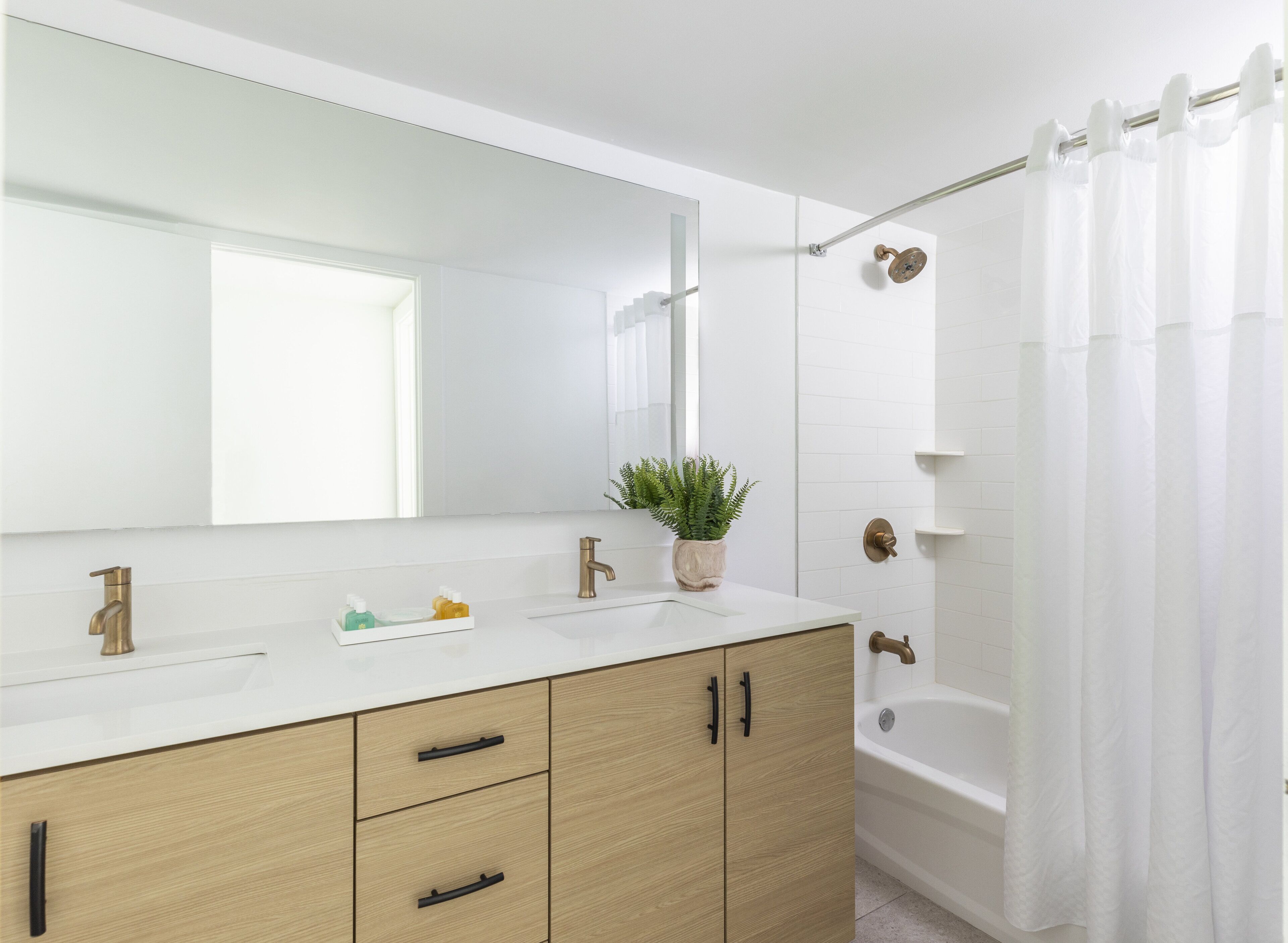 A modern bathroom with a large mirror, two sinks, a bathtub, and a shower curtain.