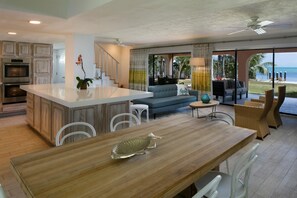 A spacious living area with a wooden dining table, a sofa, and a view of the ocean.