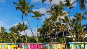 Uma fileira de cabanas de praia coloridas, com palmeiras ao fundo.