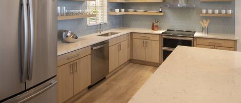 A modern kitchen with a stainless steel refrigerator, wooden cabinets, a marble countertop, and a backsplash with hexagonal tiles.
