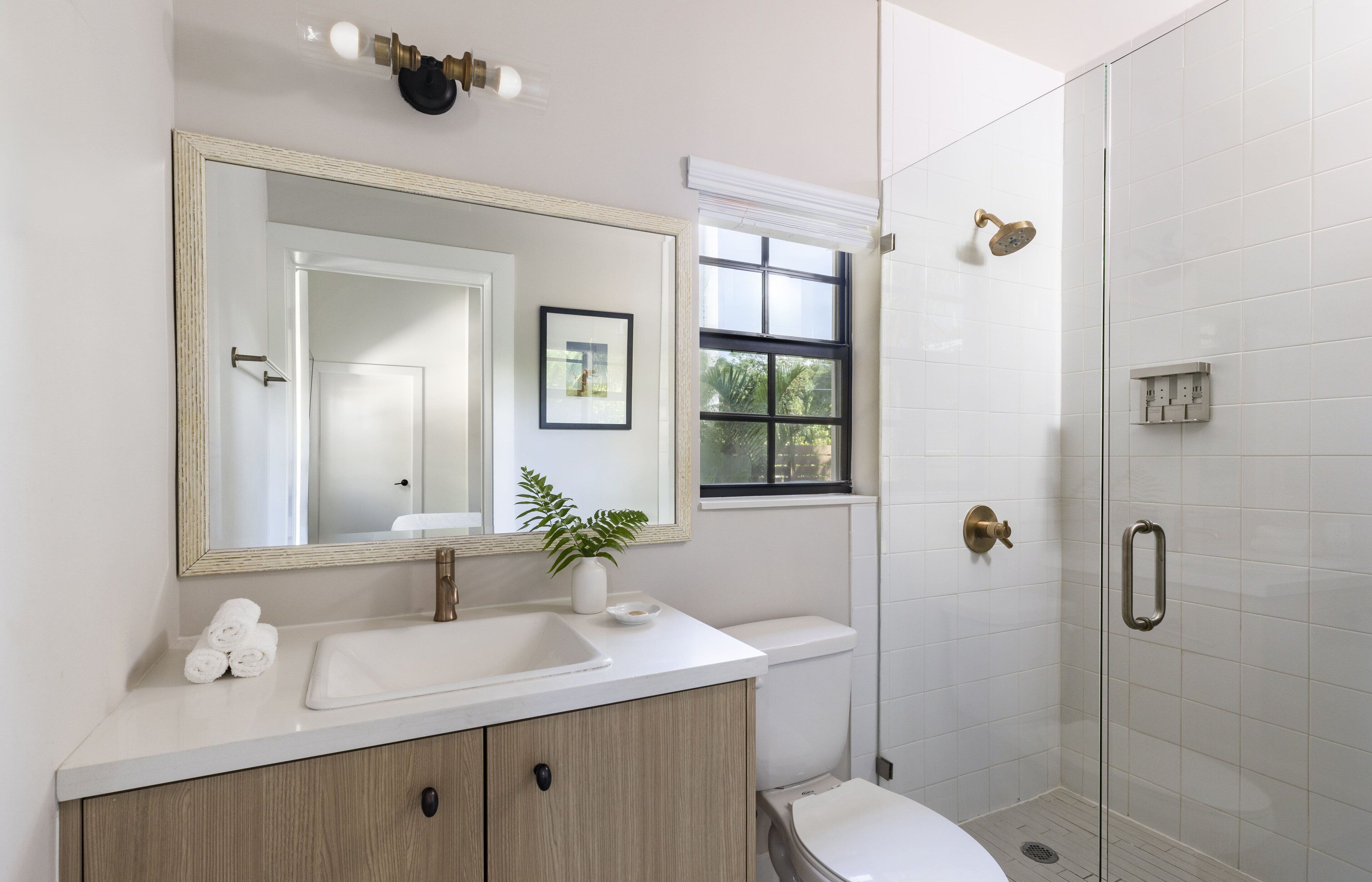 Une salle de bain moderne avec un grand miroir, un lavabo blanc, un meuble-lavabo en bois, des toilettes et une douche à parois de verre.