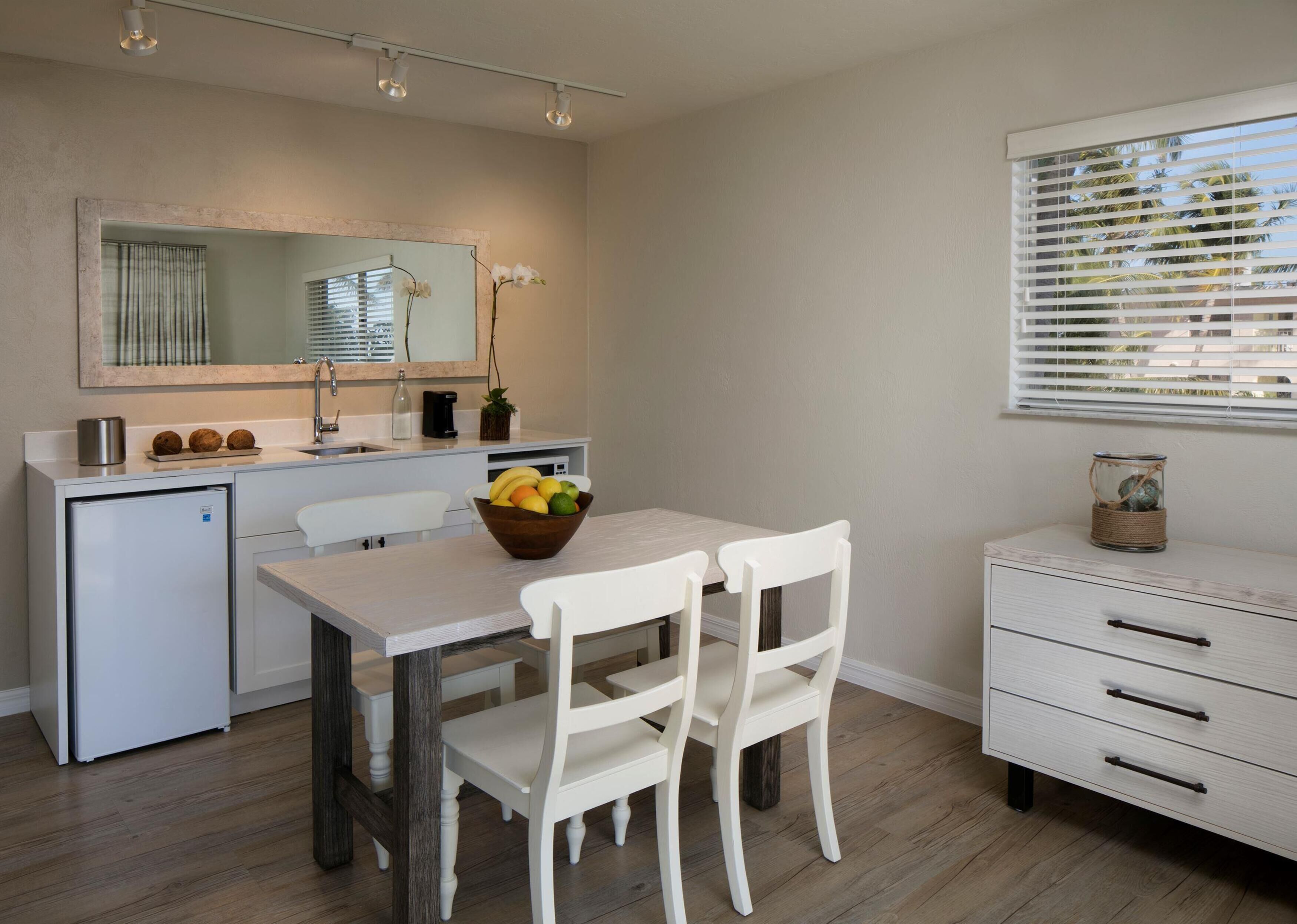 Cocina compacta con comedor, un refrigerador pequeño, un lavamanos y una ventana con persianas.
