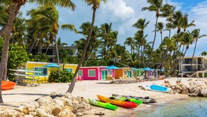 Uma praia com edifícios coloridos, caiaques e espreguiçadeiras.