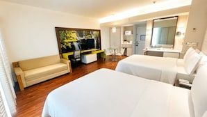 A hotel room with two beds, a sofa, a desk with a chair, a television, a mirror, and a bathroom with a sink and mirror. - BelAir Business a Wyndham Garden Hotel (Mexico City)