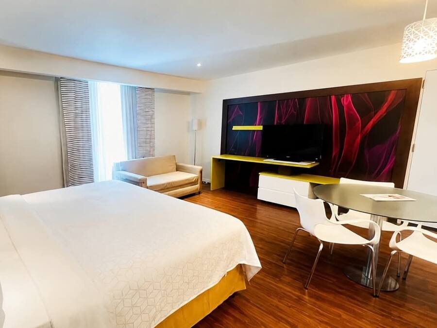 A hotel room with a large bed, a desk, a chair, and a television.
