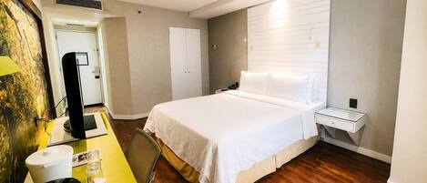 A hotel room with a bed, bedside table, and a desk with a chair.