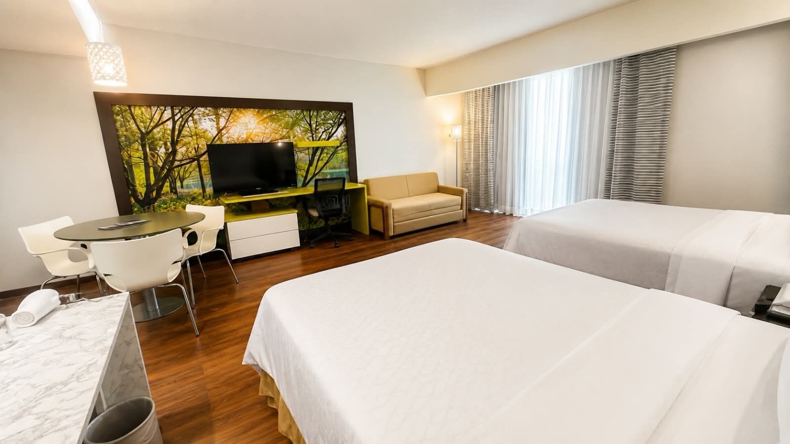 Ein Hotelzimmer mit Bett, Schreibtisch mit Fernseher, Stuhl und einem Fenster mit Vorhängen.