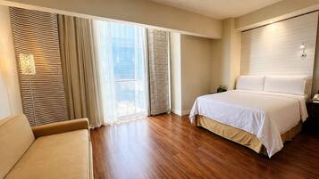 Una habitación de hotel con cama, una silla y un ventanal con cortinas.