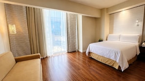 A hotel room with a bed, a chair, and a large window with curtains.