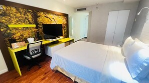 Ein Hotelzimmer mit einem Bett, einem Schreibtisch mit Computer, einem Sessel und einem Fernseher.