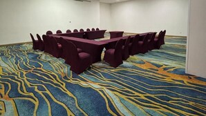 A conference room with a large oval table, purple chairs, and a patterned carpet.