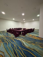 Une salle de conférence dotée d’une grande table ovale, de chaises violettes et d’un tapis à motifs.