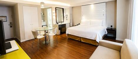 A hotel room with a bed, a desk with chairs, a mirror, a window, and a door.