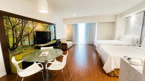 Ein Hotelzimmer mit Fernseher, einem Esstisch mit Stühlen, einer Couch, einem Bett und einem großen Fenster mit Vorhängen.