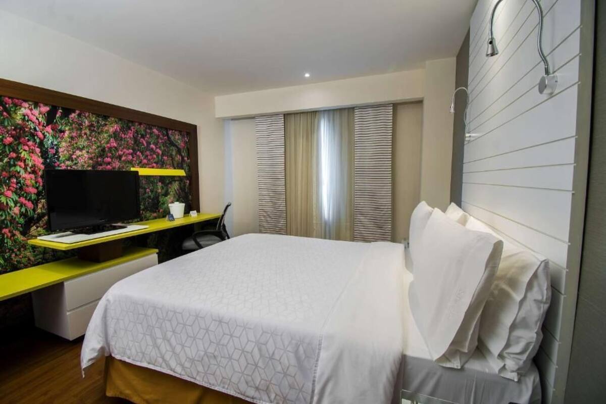 Ett hotellrum med en säng, ett skrivbord med en tv och en dusch.