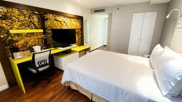A hotel room with a bed, a desk with a computer, a television, and a wardrobe.