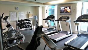 Une salle de sport équipée de tapis de course, d’un appareil elliptique et d’haltères.