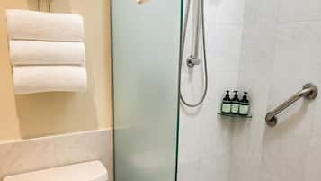 Un baño con ducha de vidrio, inodoro y toallero con toallas dobladas.