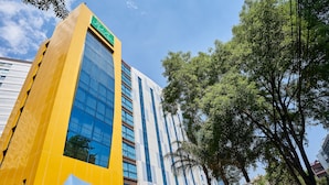 Een modern hotelgebouw met een gele gevel en een groen bord.