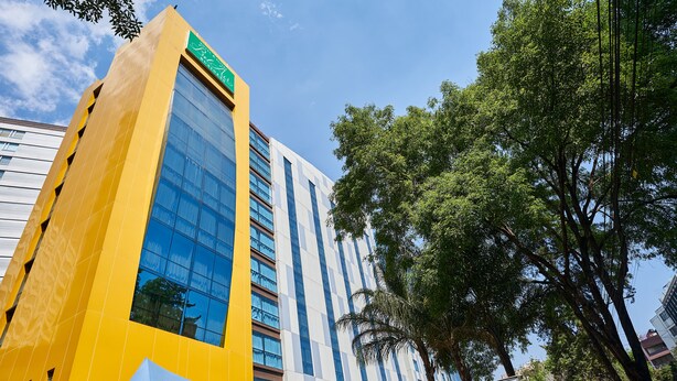 A modern hotel building with a yellow facade and a green sign.