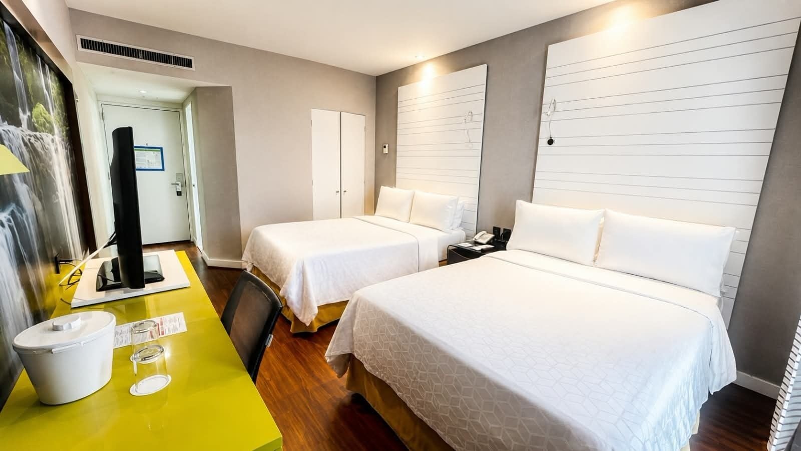 Habitación de hotel con dos camas, un escritorio con computadora y un baño con ducha.