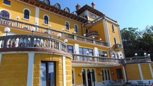 A multi-story yellow building with balconies, large windows, and a well-maintained lawn. - Grand Hotel Astoria (Lavarone)
